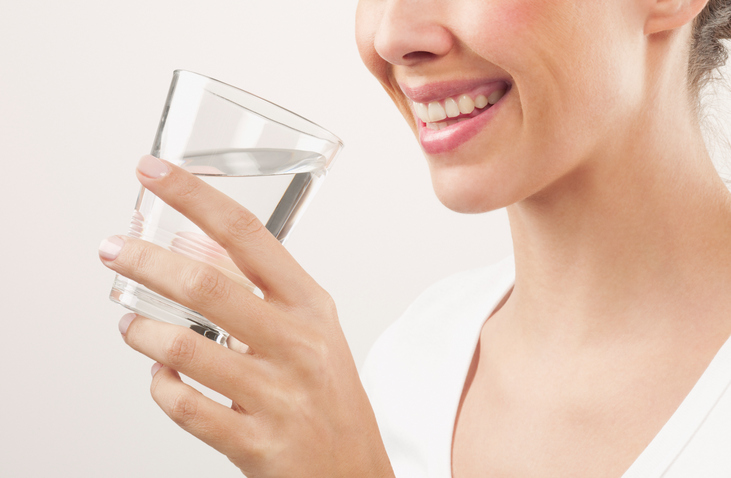 Smiling woman drinking a glass of tap water.