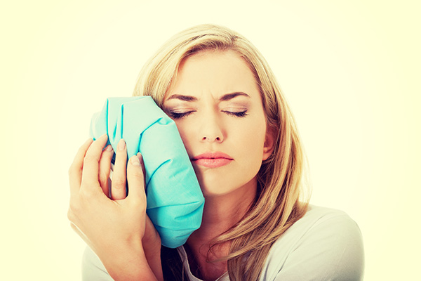 Woman with a toothache holding an ice pack to her cheek.