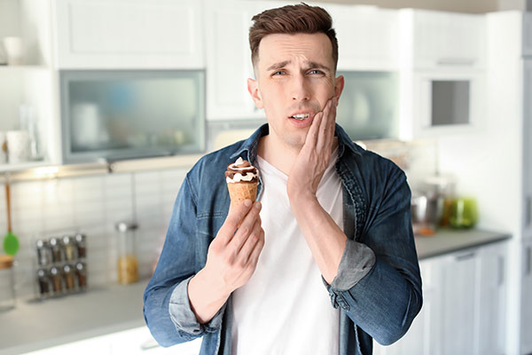 A man eating ice cream experiencing tooth pain due to loss of enamel.