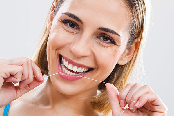 A flossing woman with signs of healthy teeth.