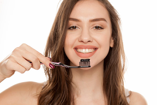 A woman with activated charcoal toothpaste on her toothbrush.