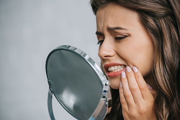 A woman with dental health issues inspecting her mouth with a mirror.