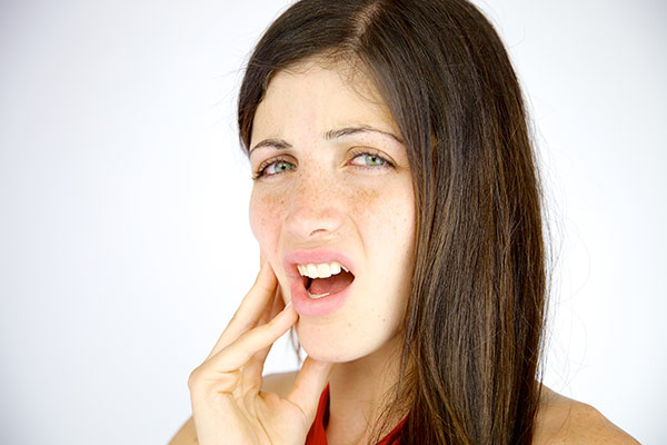 A woman with tooth abscess pain holding her cheek.
