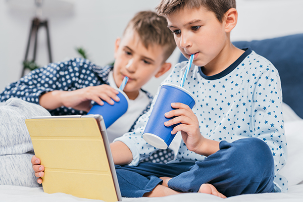 Two children sipping soda from cups, leading to cavity prone teeth.