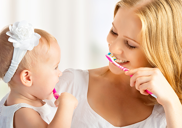 A mother showing her child how to brush to help in caring for her baby teeth.