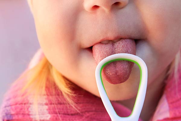 Child using a tongue scraper to brush their tongue.