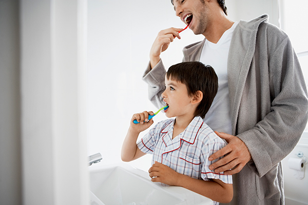 A father showing his son the proper way to brush teeth.