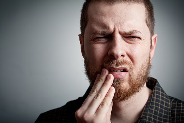 A man holds his mouth in pain, possibly from bleeding gums. Walbridge Dental addresses the cause of bleeding gums.