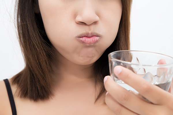A woman oil pulling for dental care with a glass of water to rinse