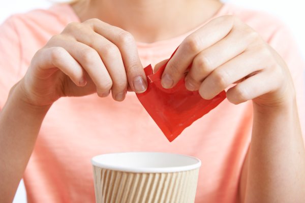 A woman tears open a packet of artificial sweetener for her beverage. Do artificial sweeteners cause tooth decay?