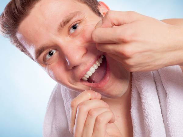 A man flossing his teeth and wondering why his gums are bleeding.
