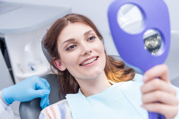 A woman checking her teeth in a mirror at the dentist