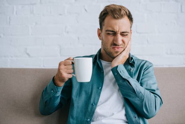 A man wincing in pain with coffee, wondering "why are my teeth sensitive?"