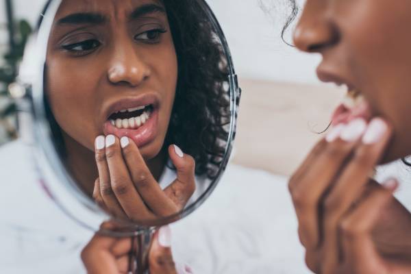 A worried young woman looks in a mirror at the reflection of her teeth and wonders, “I chipped my tooth, what should I do?”