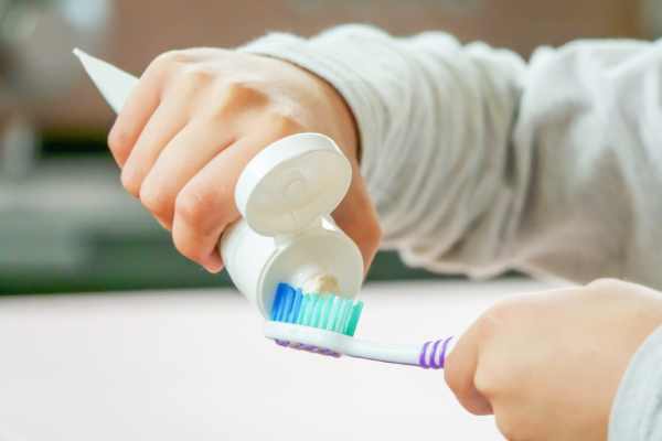 A person holding one type of toothpaste in their hand, squeezing it on to a toothbrush